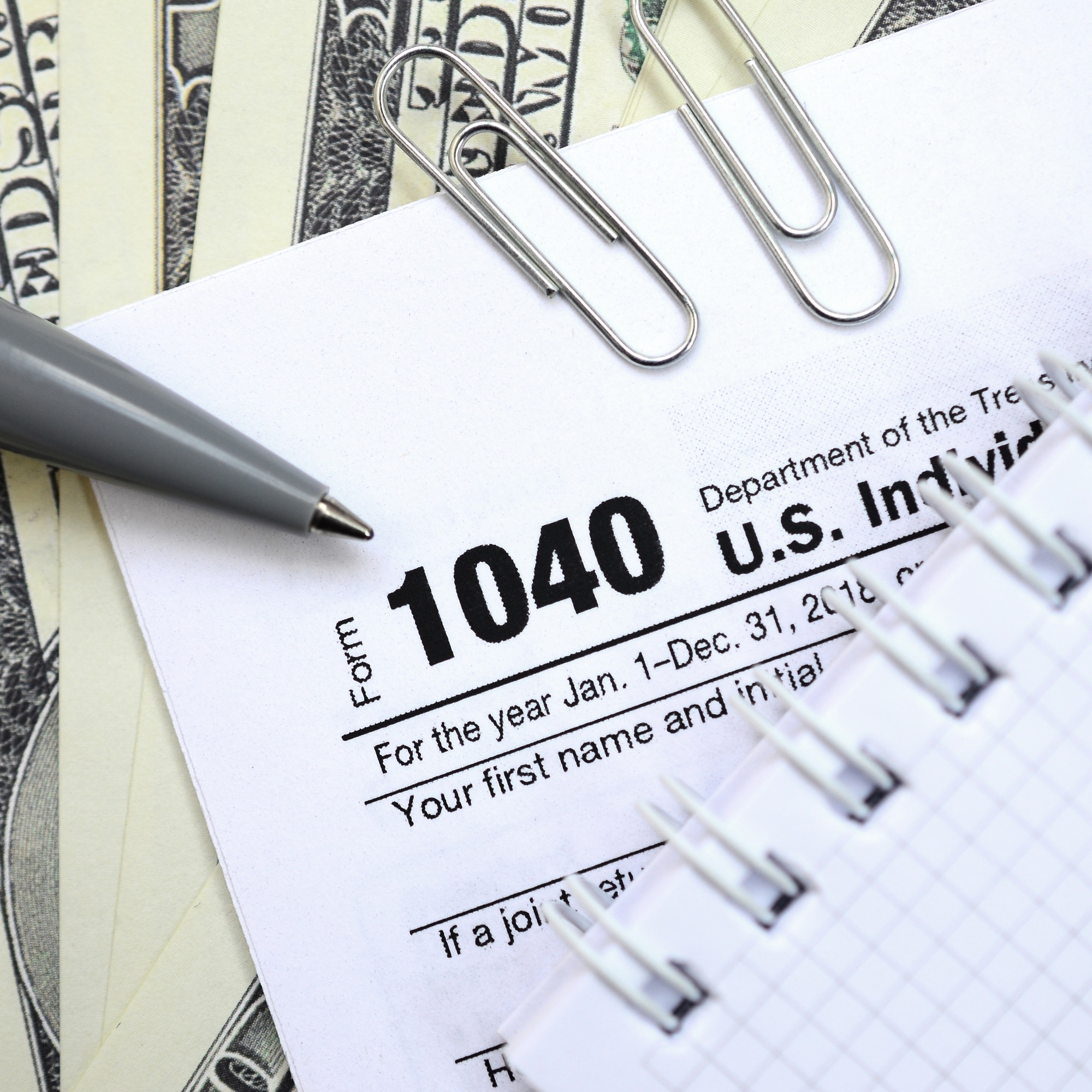 The pen, notebook and dollar bills is lies on the tax form 1040 U
